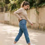 image of a young woman walking while subtly pulling up the waistband of her jeans. Slight gap visible at the back of the waistband to clearly show the slipping problem. Natural body movement, casual everyday outfit, confident but slightly frustrated expression.